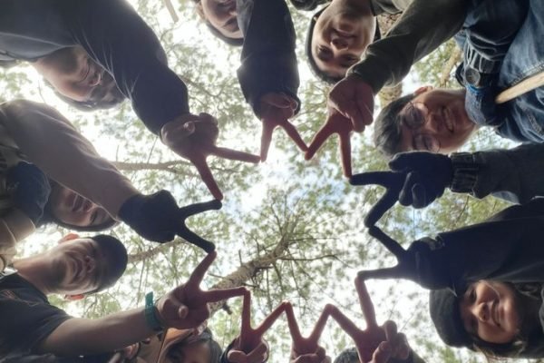 A diverse group of friends creatively form a star shape with their fingers while standing outdoors.